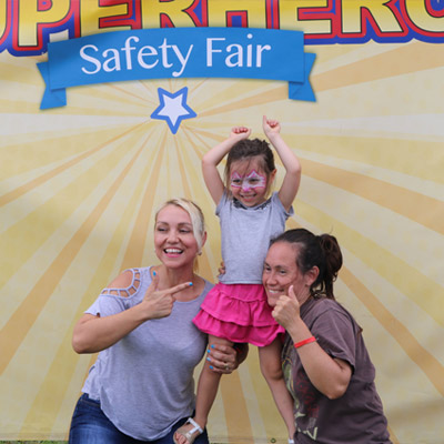 two women and child posing for picture at superhero event
