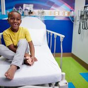 boy smiling sitting on bed in pediatric hospital room